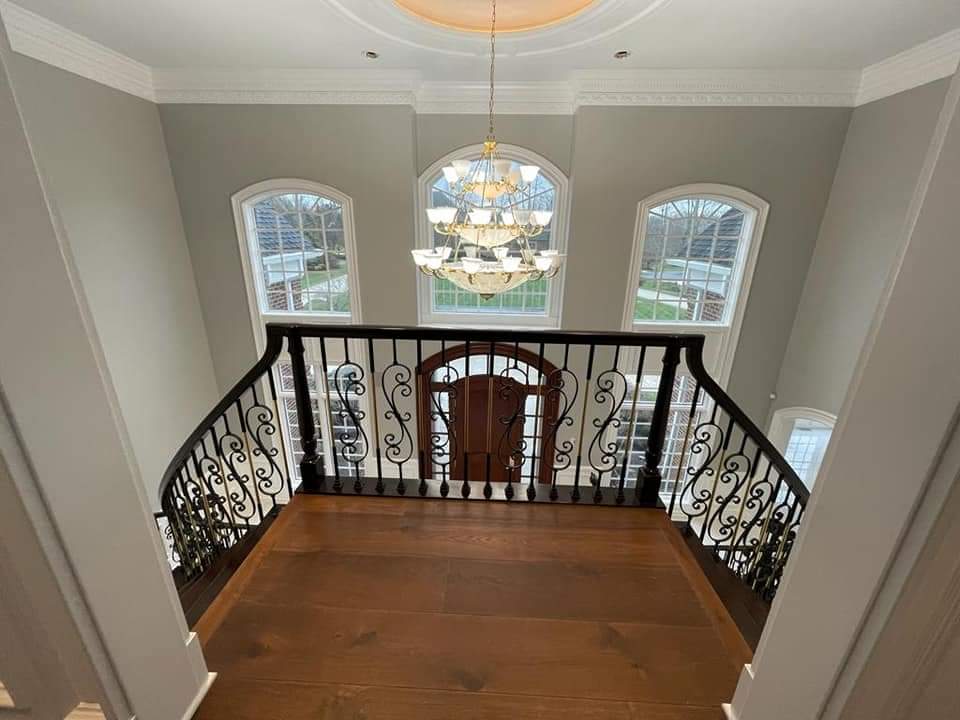 View from a landing overlooking a grand foyer with a chandelier, windows, and ornate railings.