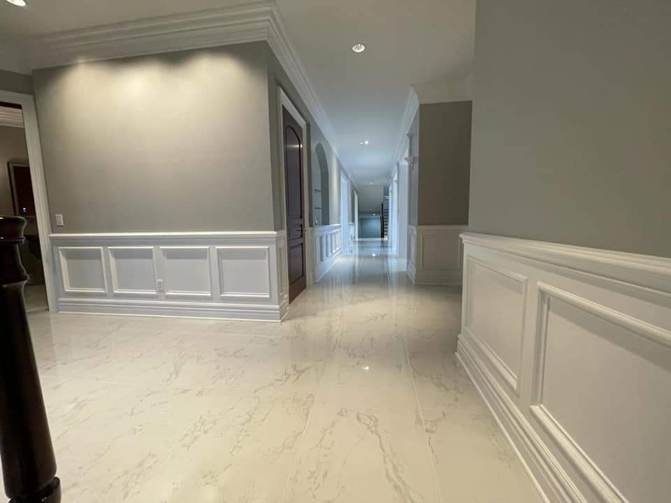 Long hallway with white paneled walls, gray paint, and marble-like floor.