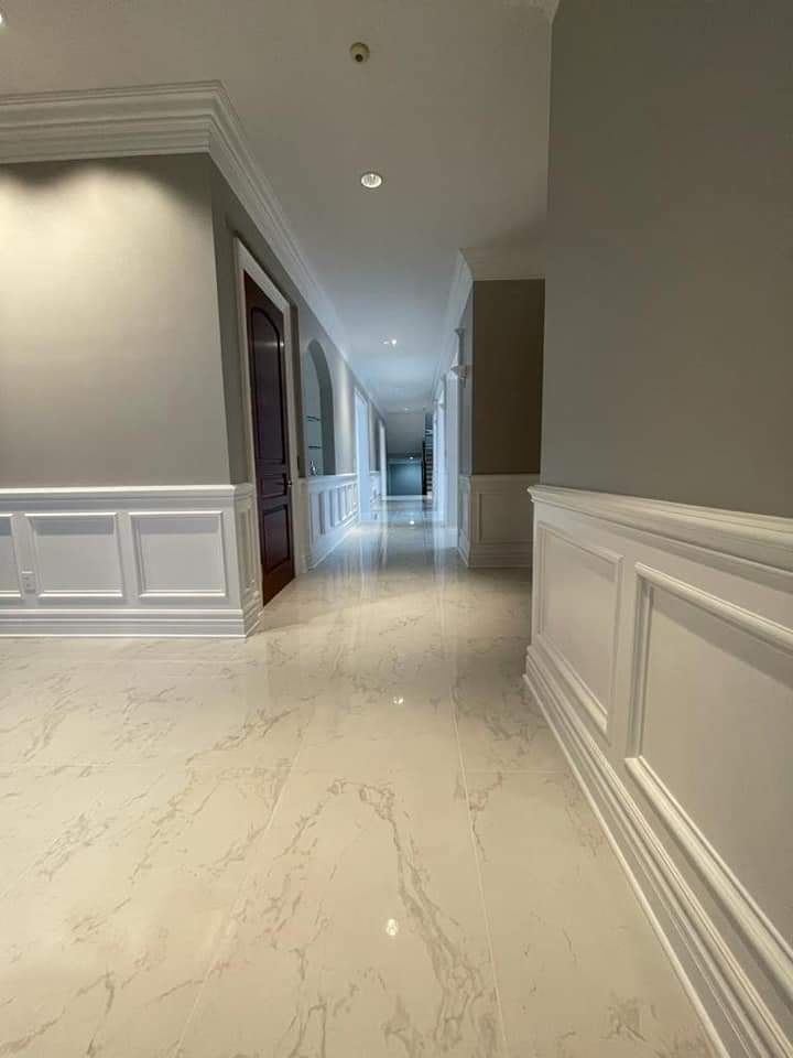 Long hallway with white paneling and marble-like floor, leading to a dark door.