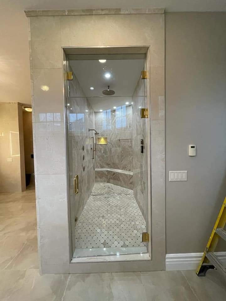 Spacious bathroom with glass shower door, marble tile walls and floor, gold fixtures, recessed lighting.