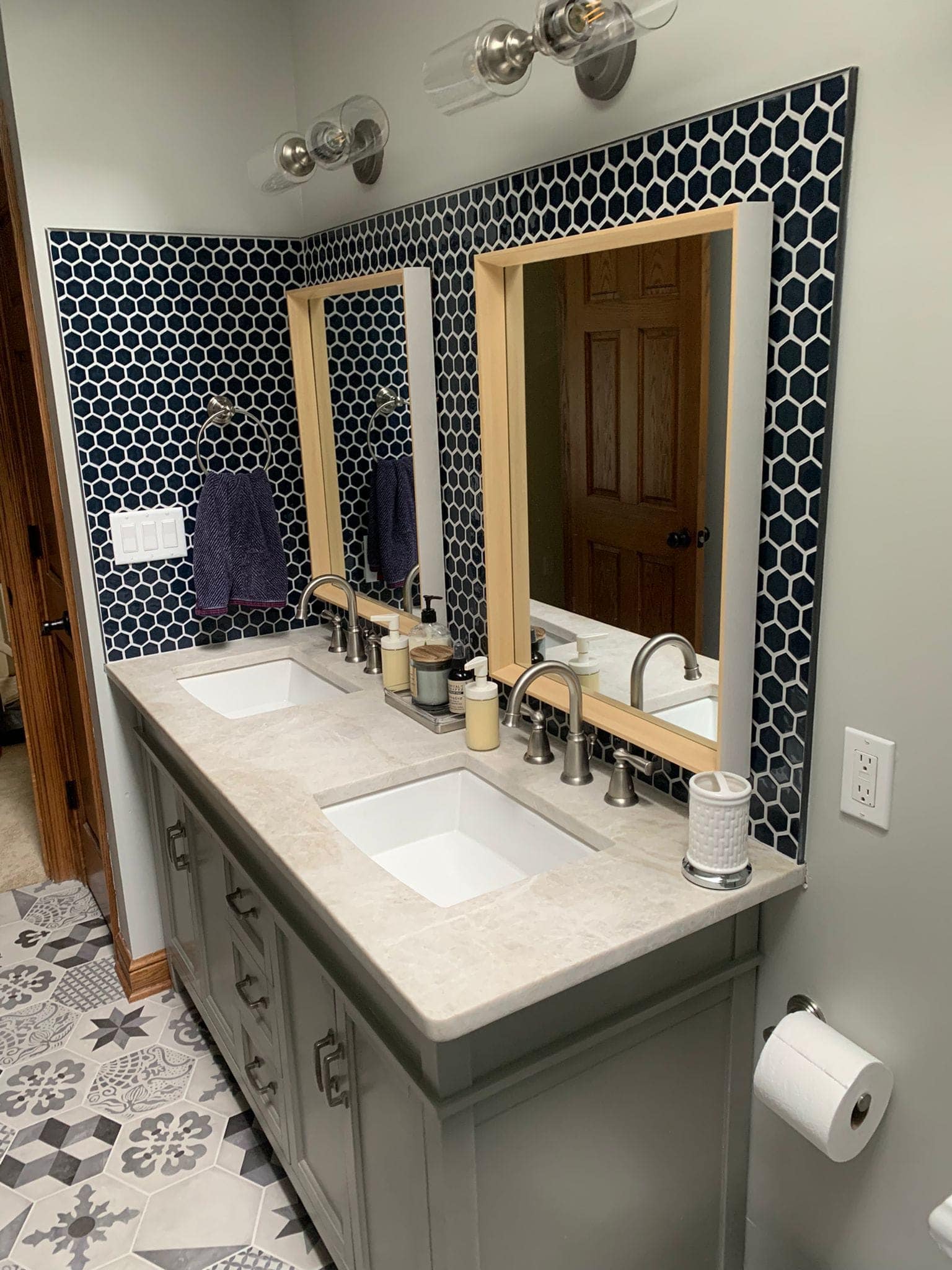 Bathroom with a double vanity. Navy and white tile backsplash, light wood mirrors, and gray vanity.