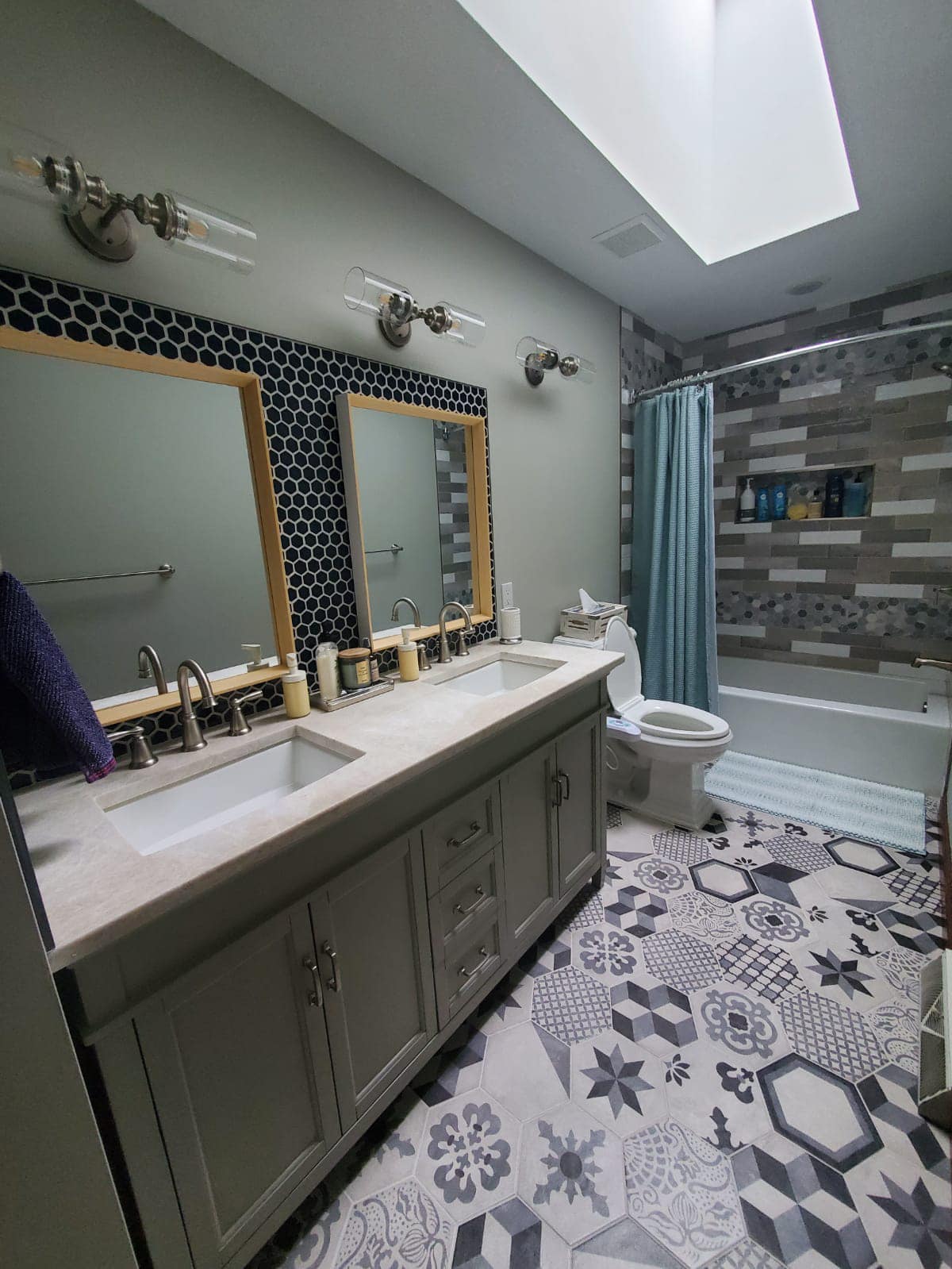 Bathroom with double sinks, tiled floor, shower, and skylight. Gray and blue color scheme.