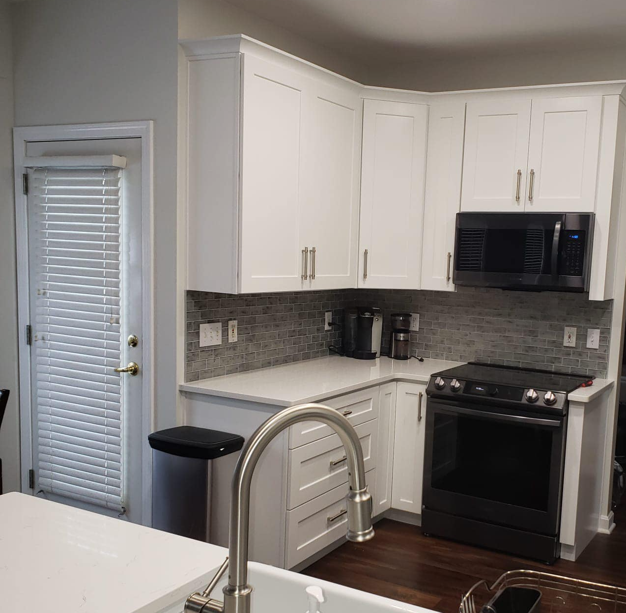 White kitchen cabinets with black appliances, a sink, and a door with blinds.