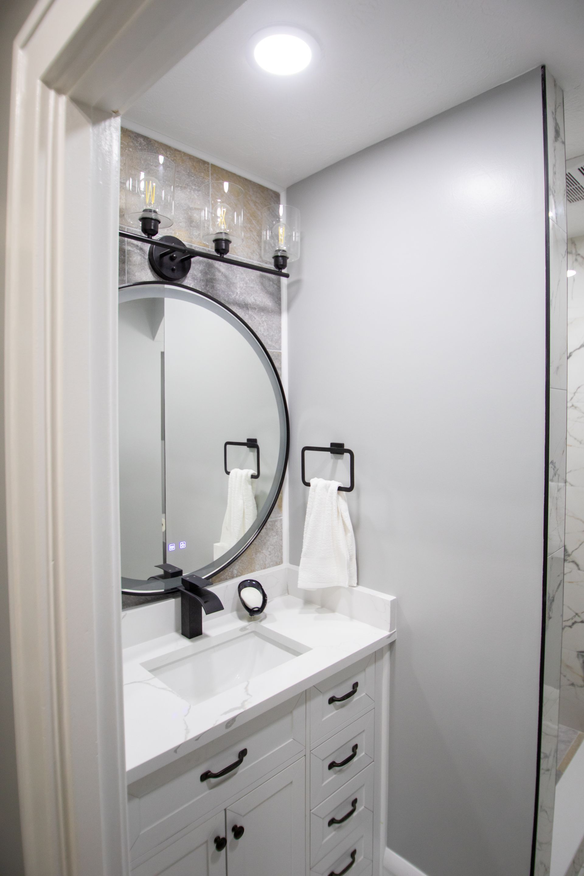 Modern bathroom with a white vanity, round mirror, and black fixtures.