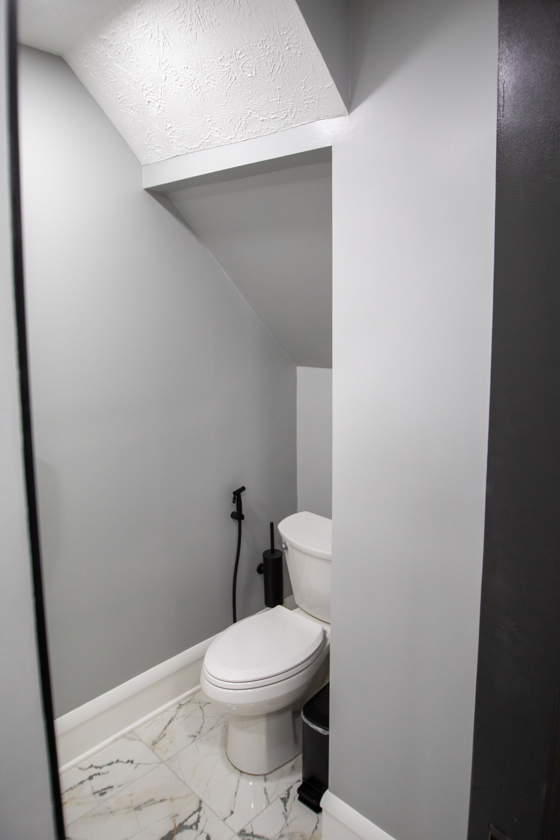 Small, grey bathroom with a toilet, bidet, and marble floor beneath a sloped ceiling.