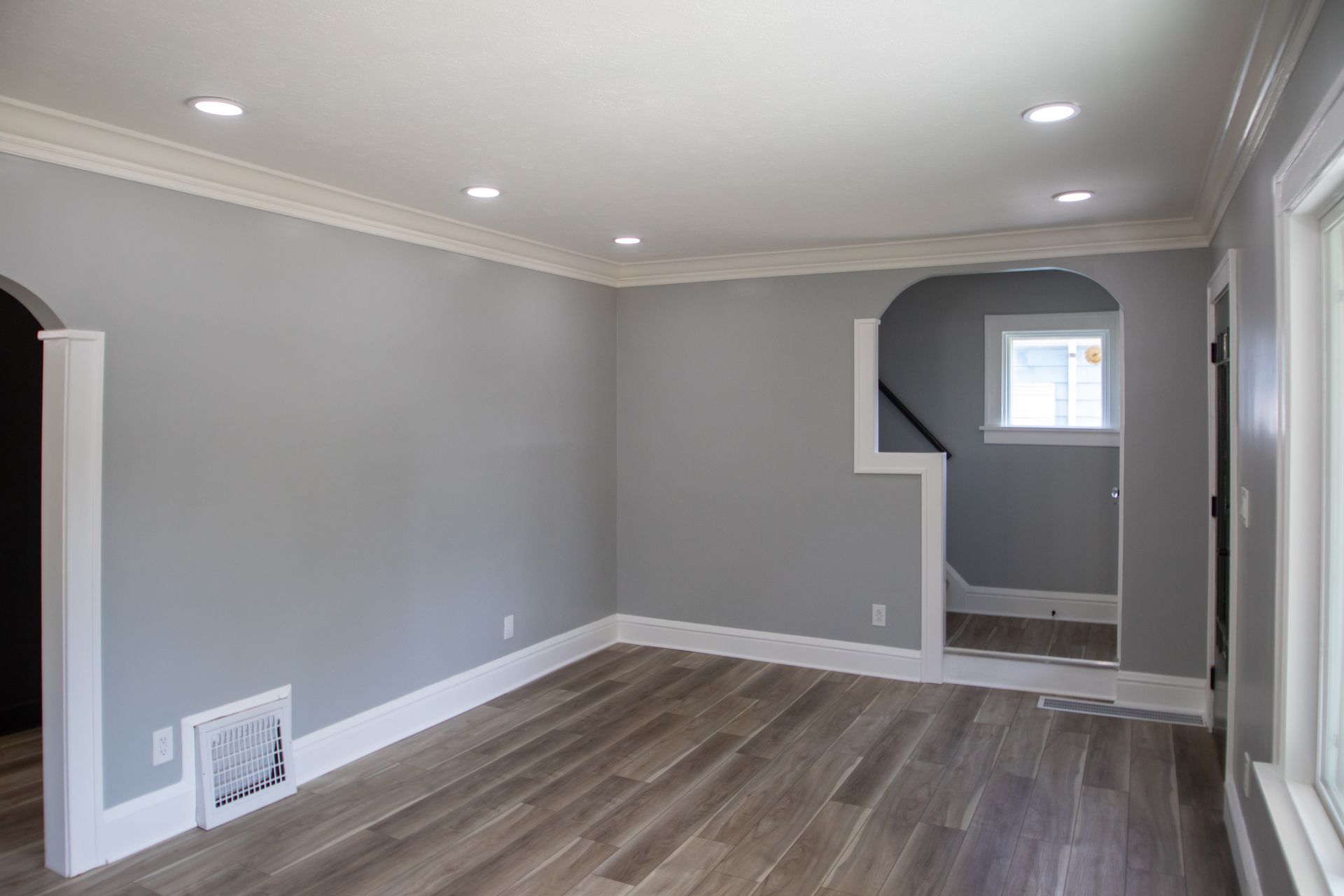 Empty room with gray walls, white trim, recessed lighting, and wooden floors.