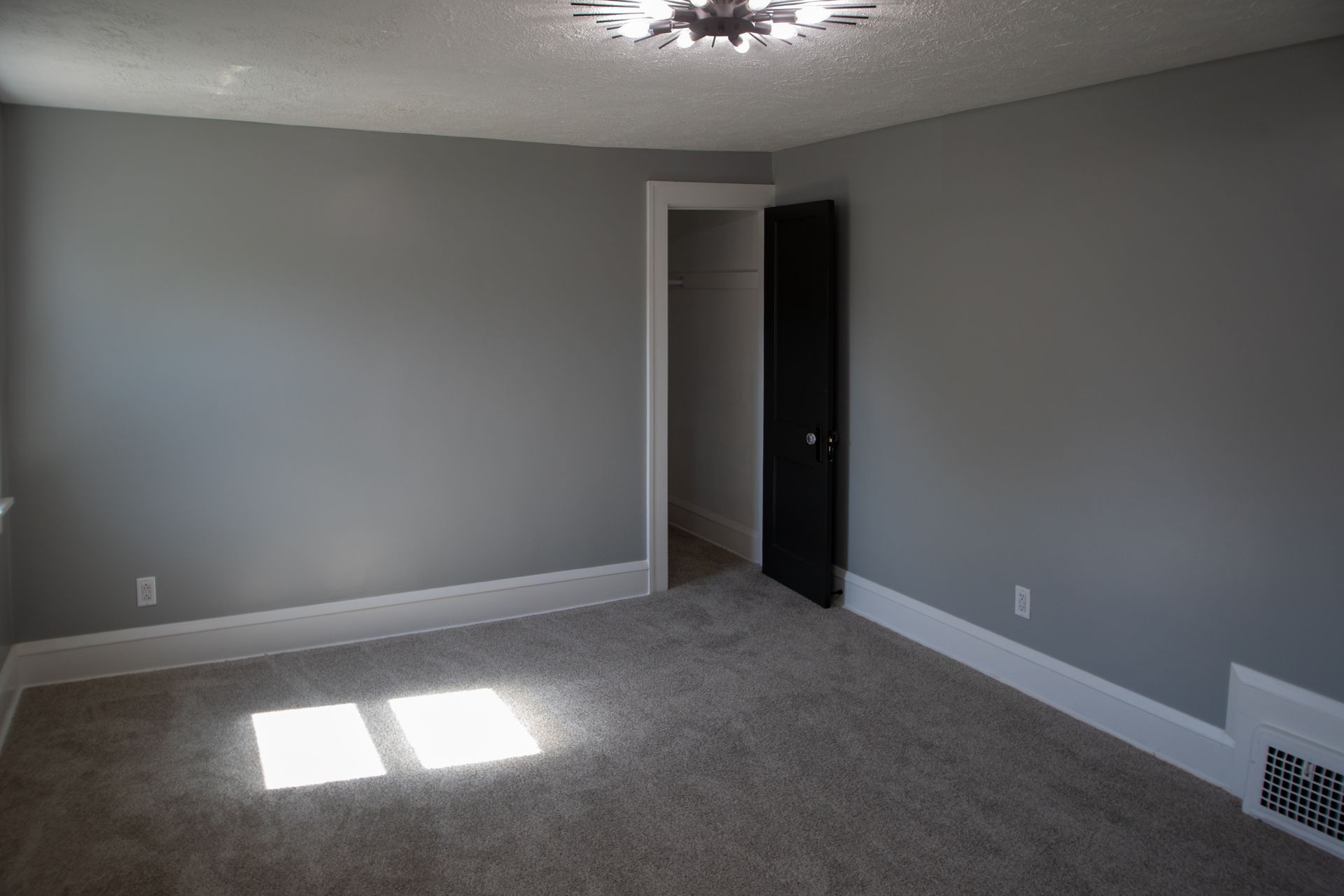 Empty bedroom with gray walls, white trim, and a black closet door.