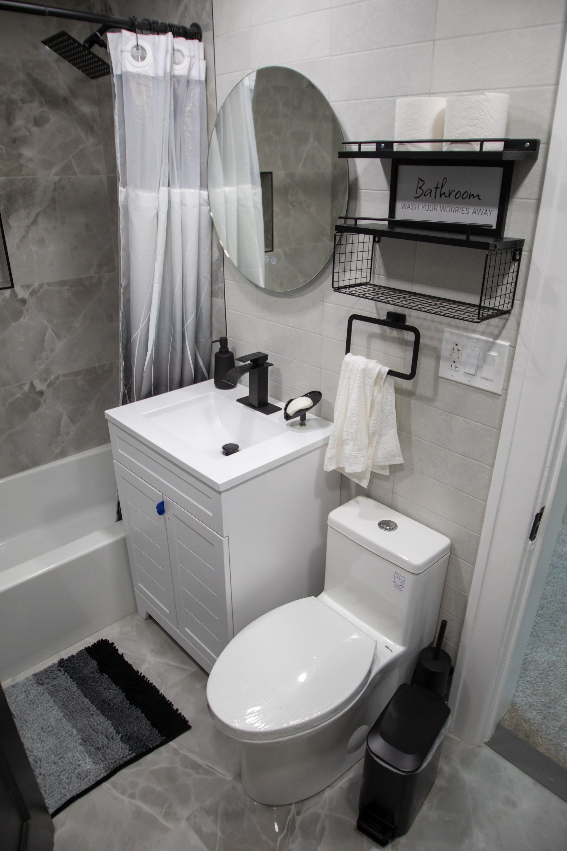 Small modern bathroom with white vanity, toilet, and black fixtures. Gray and white color scheme.