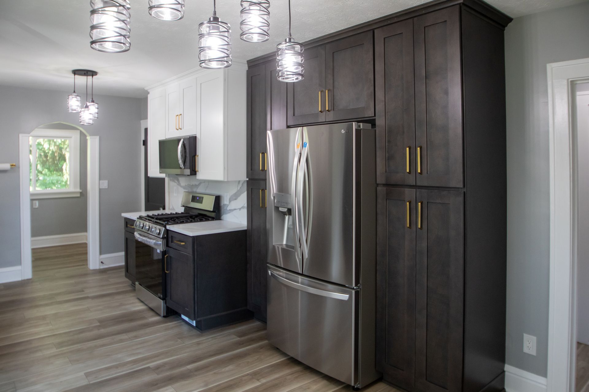 Modern kitchen with gray cabinets, stainless steel appliances, and wood-look flooring.