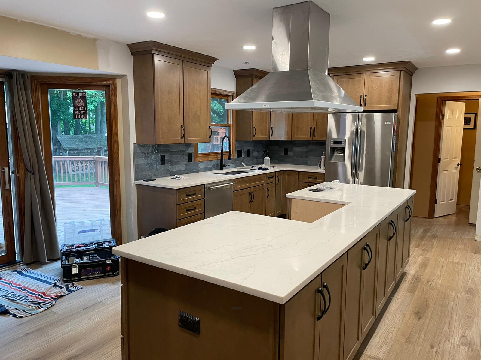 A remodeled kitchen with wooden cabinets, a large island, stainless steel appliances, and a view of a deck.