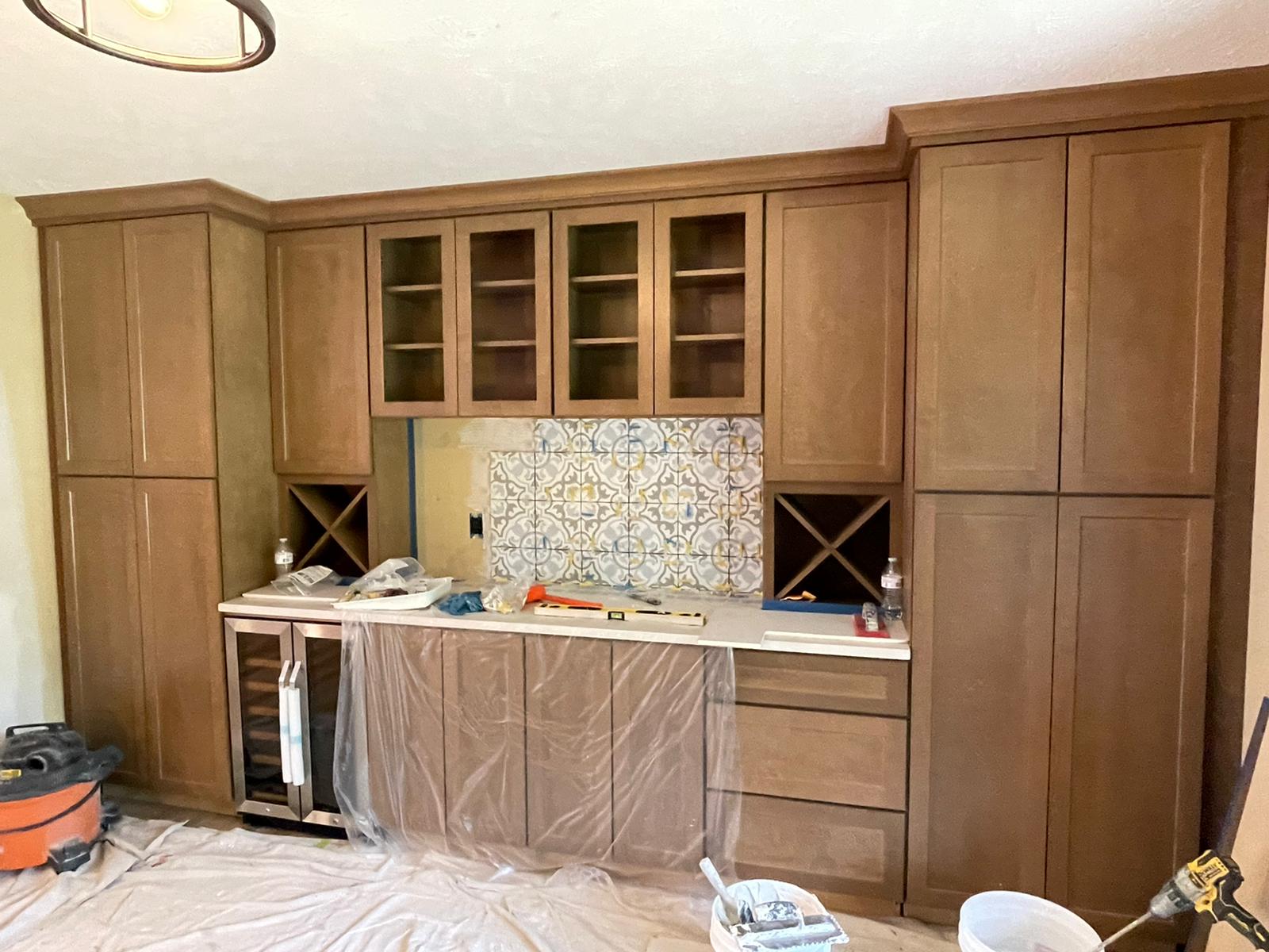 Built-in, light-brown wooden bar with cabinets, wine racks, and a tiled backsplash, during construction.
