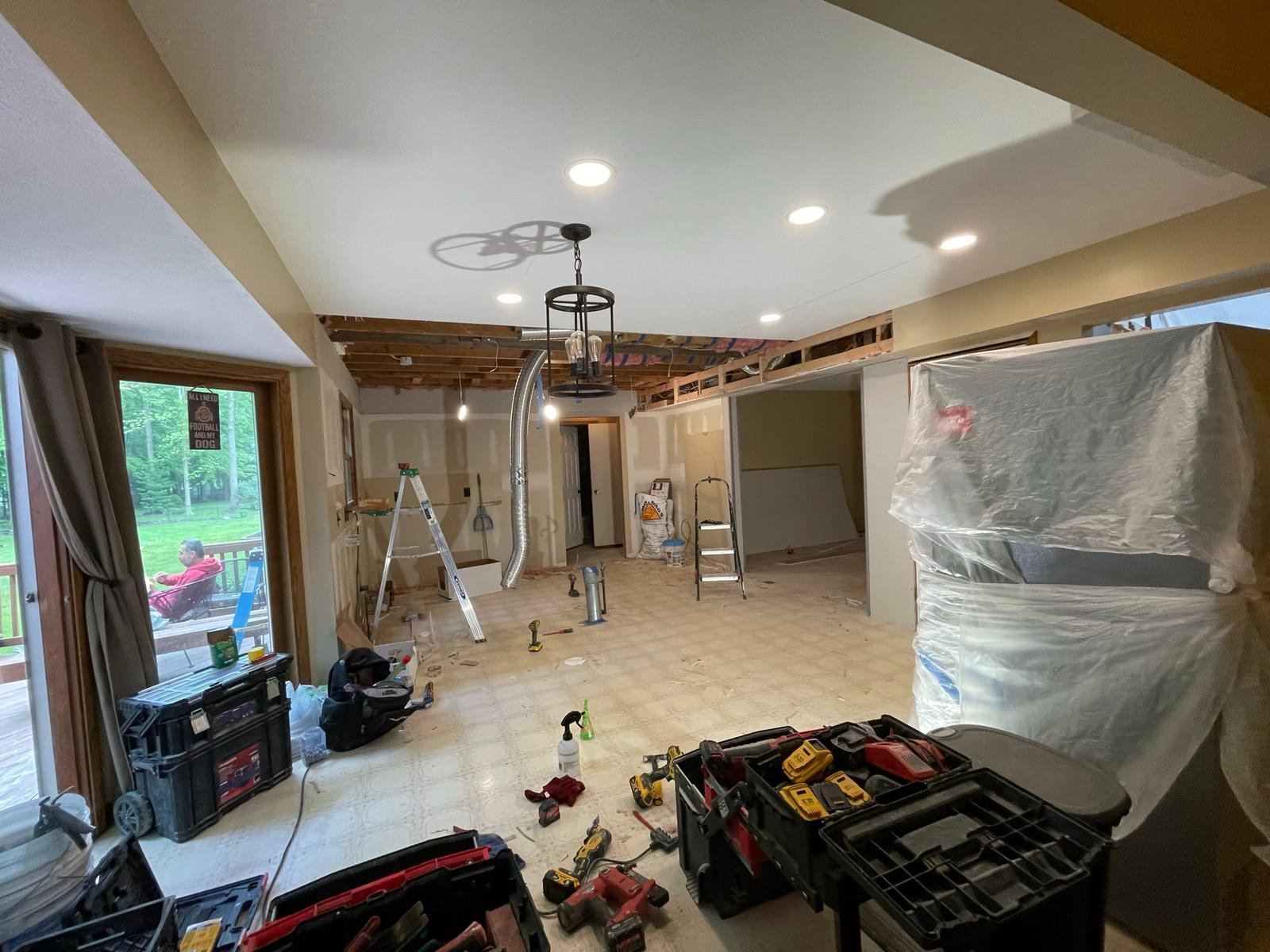 Interior undergoing renovation: exposed ceiling beams, tools and materials scattered on floor, bright lighting.