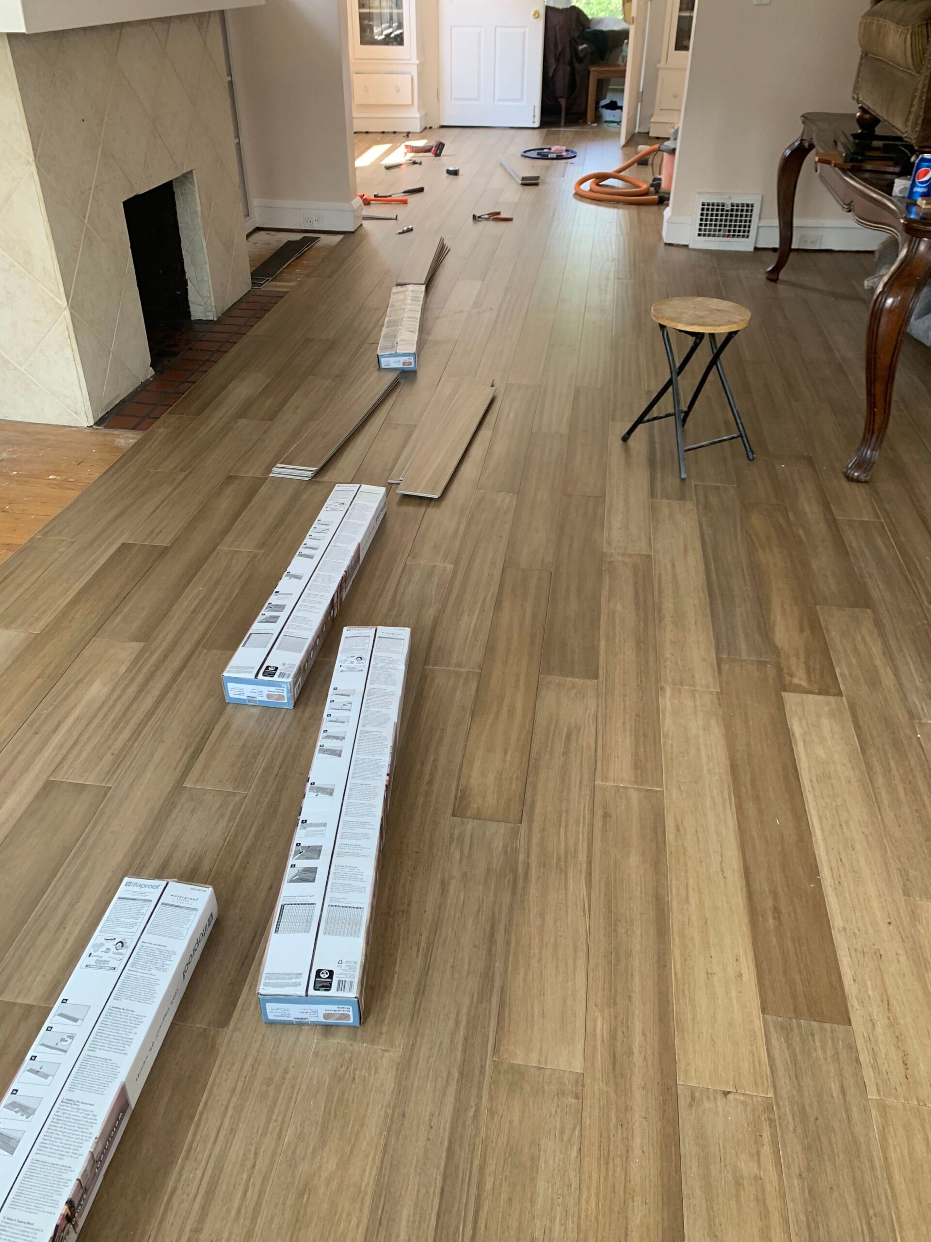 Wood flooring installation in progress; boxes of planks lie on installed floor, fireplace on left.
