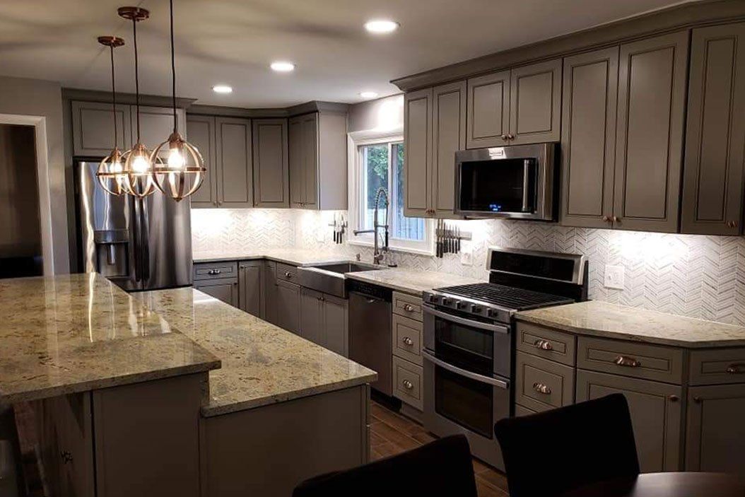 A modern kitchen with grey cabinets, granite countertops, and stainless steel appliances.
