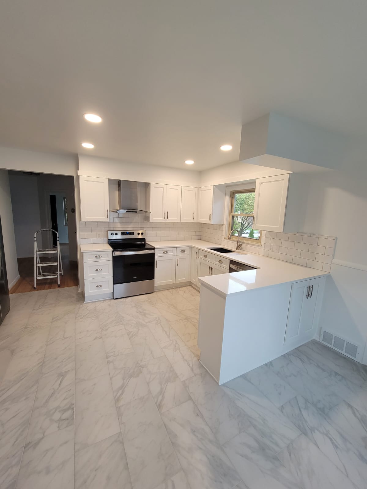 Modern white kitchen with stainless steel appliances, marble-look floor and countertops, recessed lighting.