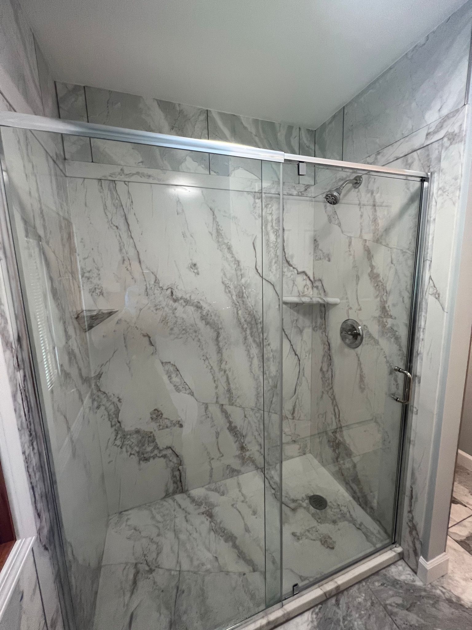 Modern shower with marble-look tiles and clear glass doors, chrome fixtures, and a recessed shelf.