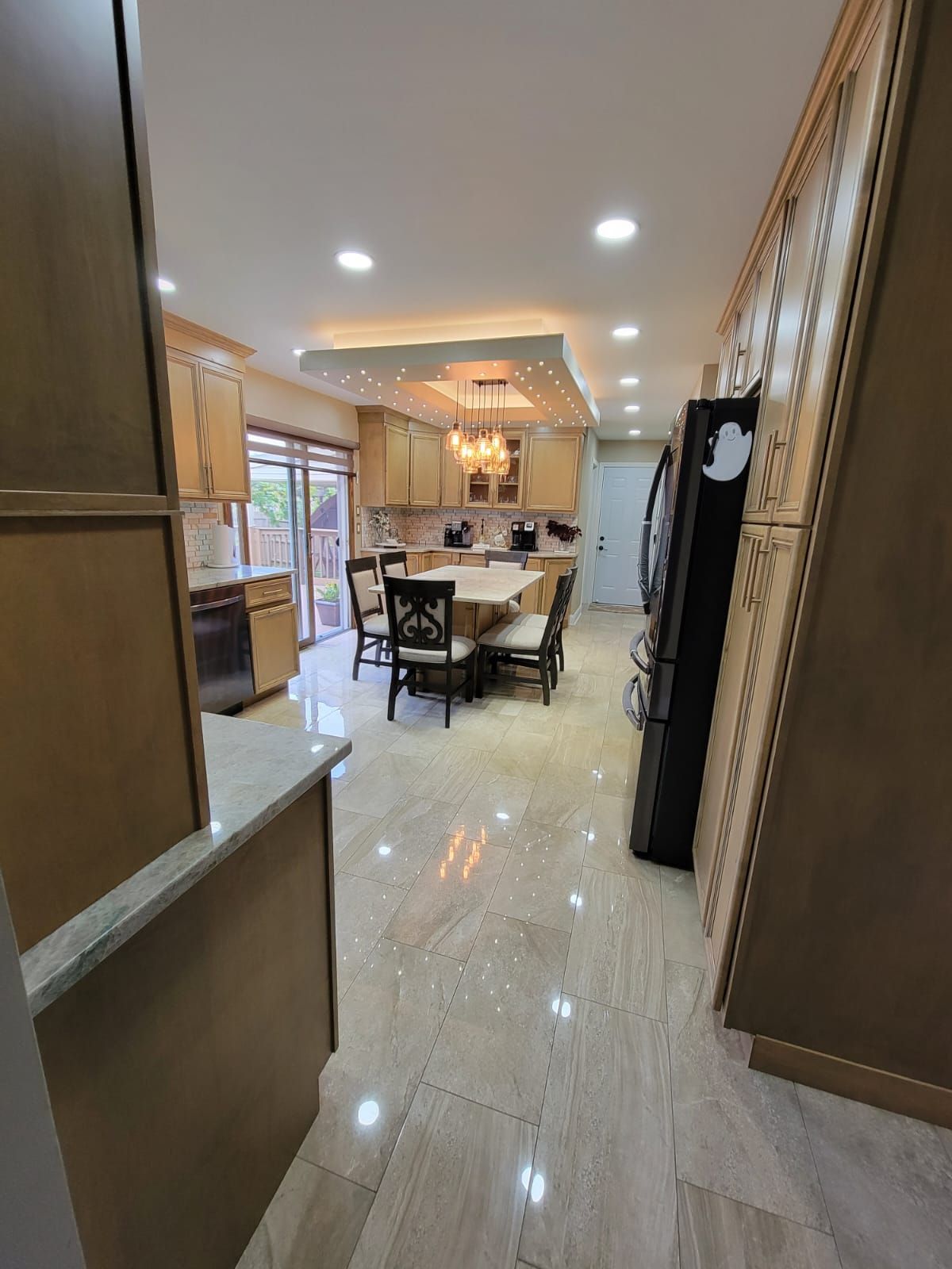 Kitchen interior with tan cabinets, marble floors, dining table, and black appliances.