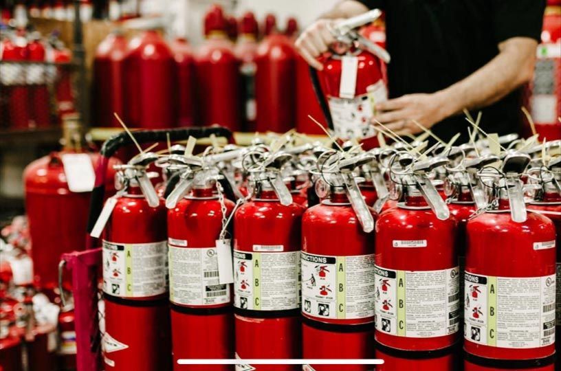 A man is holding a fire extinguisher in front of a stack of fire extinguishers.