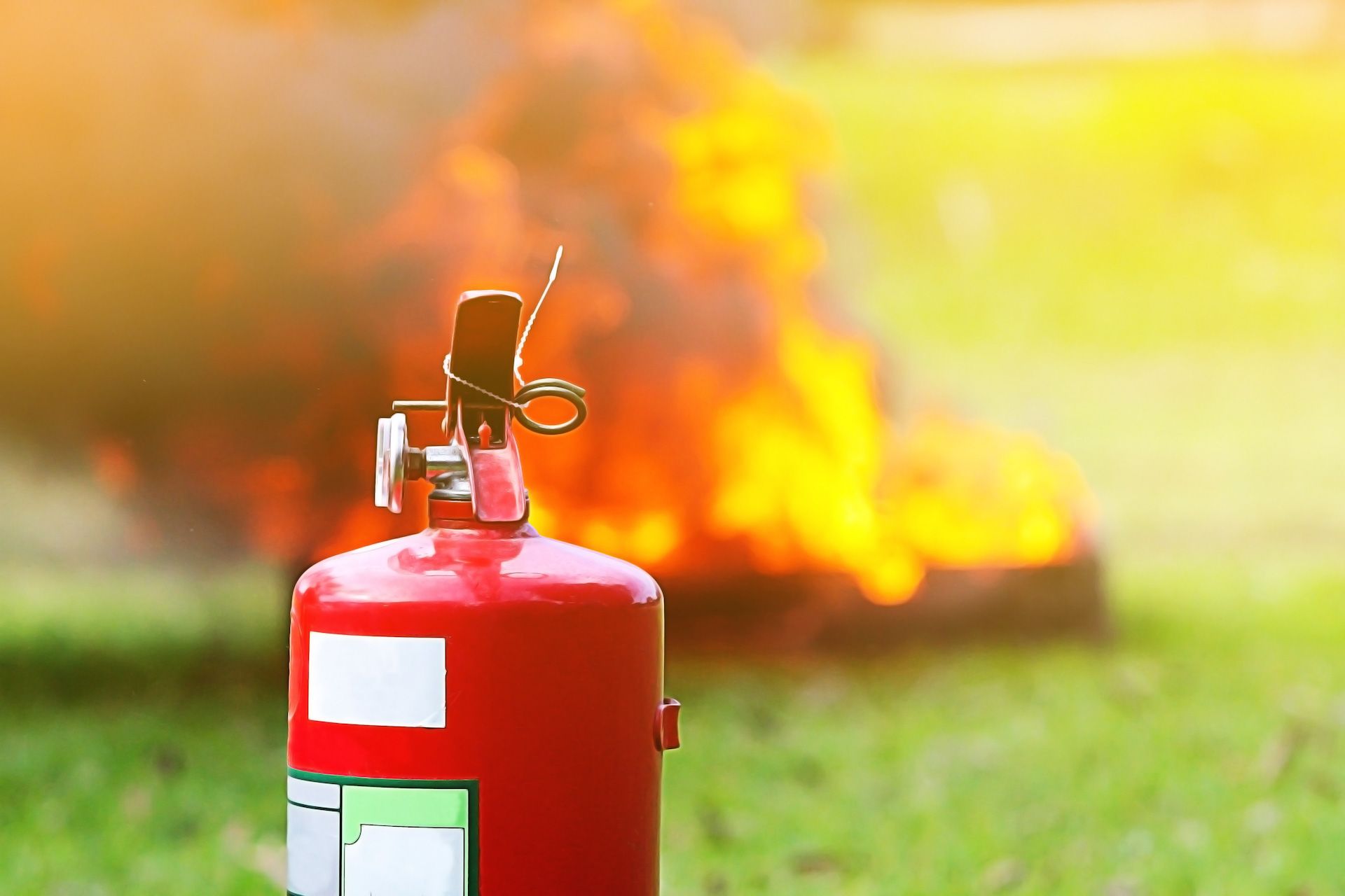 A fire extinguisher is sitting in the grass in front of a fire.