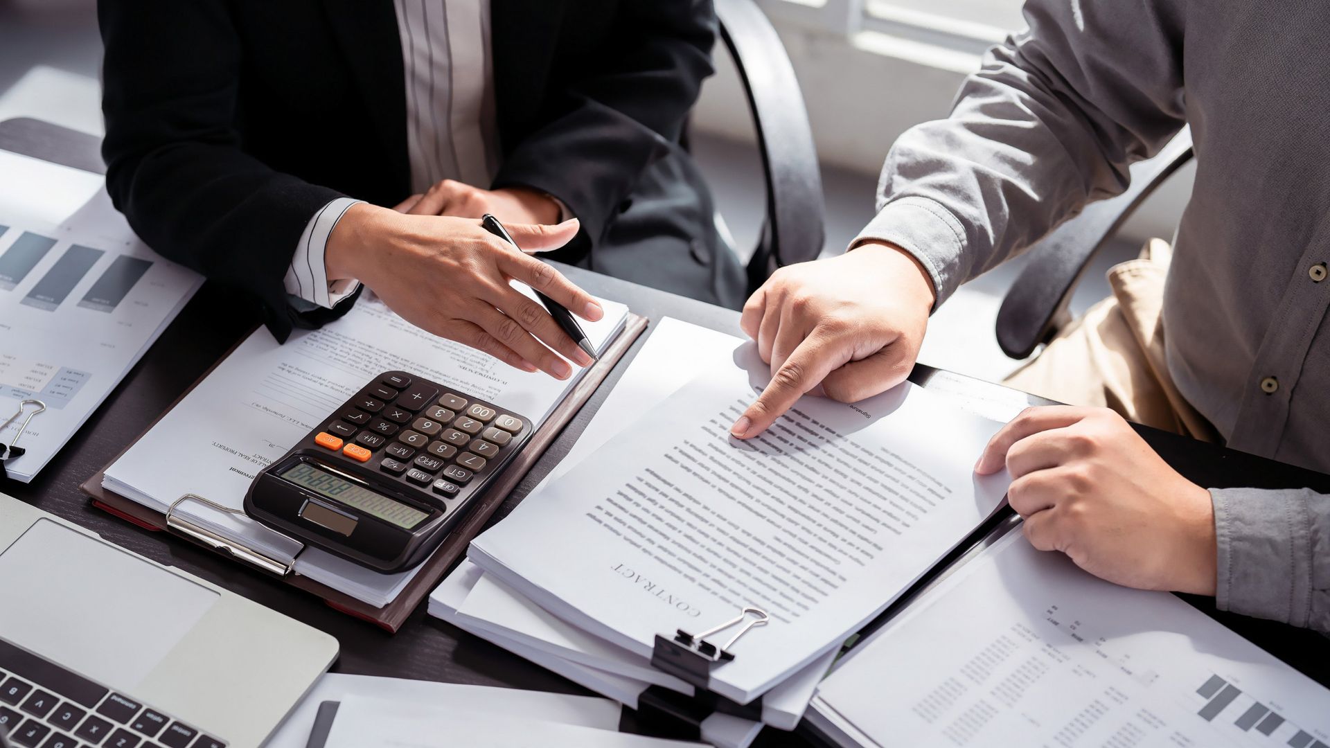 Two people reviewing documents at a desk, one pointing, calculator nearby.
