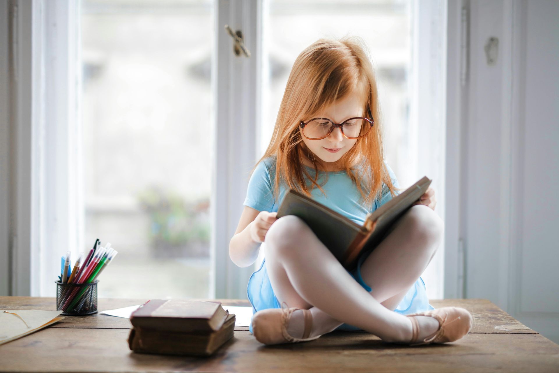 A little girl is sitting at a table reading a book.