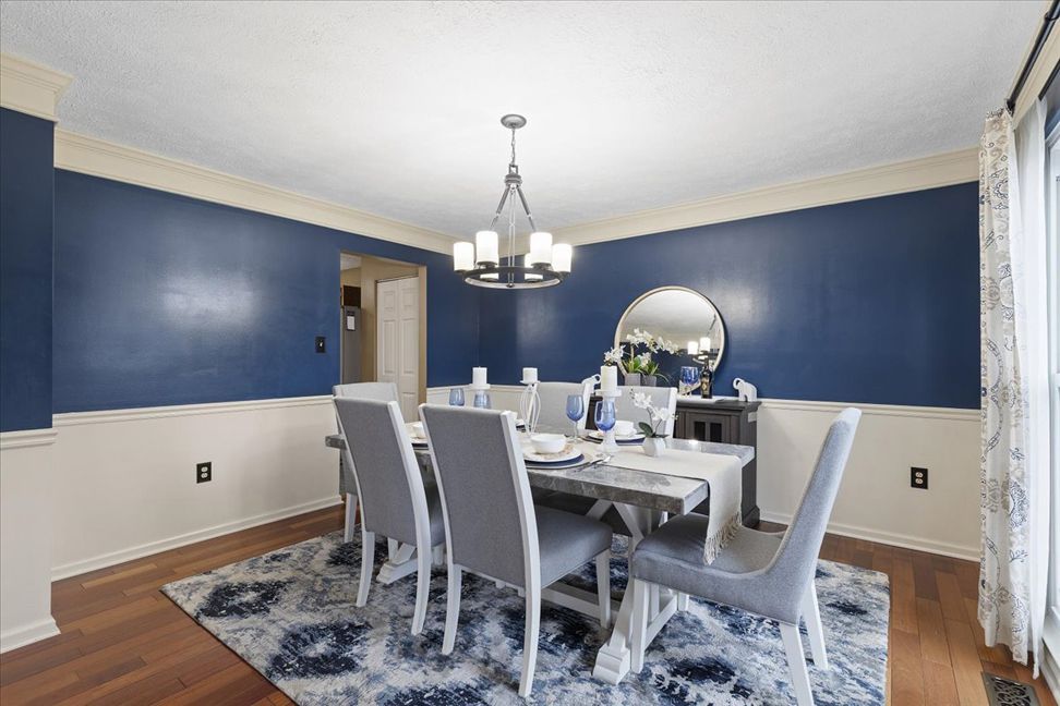 Dining room with blue walls, cream trim, wooden floor, table, chairs, and rug.