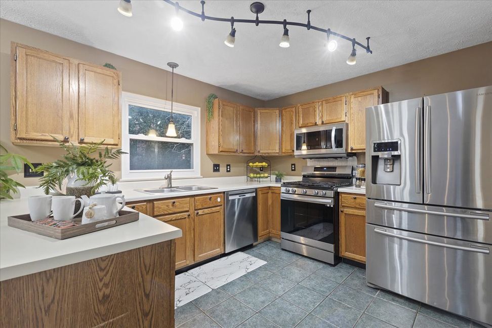 Kitchen with light wood cabinets, stainless steel appliances, and gray tiled floor.