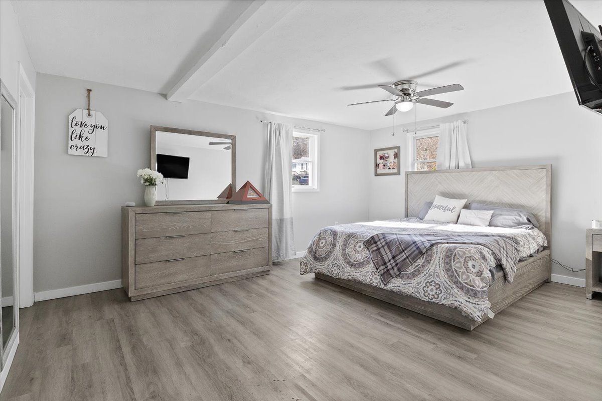 Bedroom with a bed, dresser, mirror, and ceiling fan. Light gray walls and flooring.