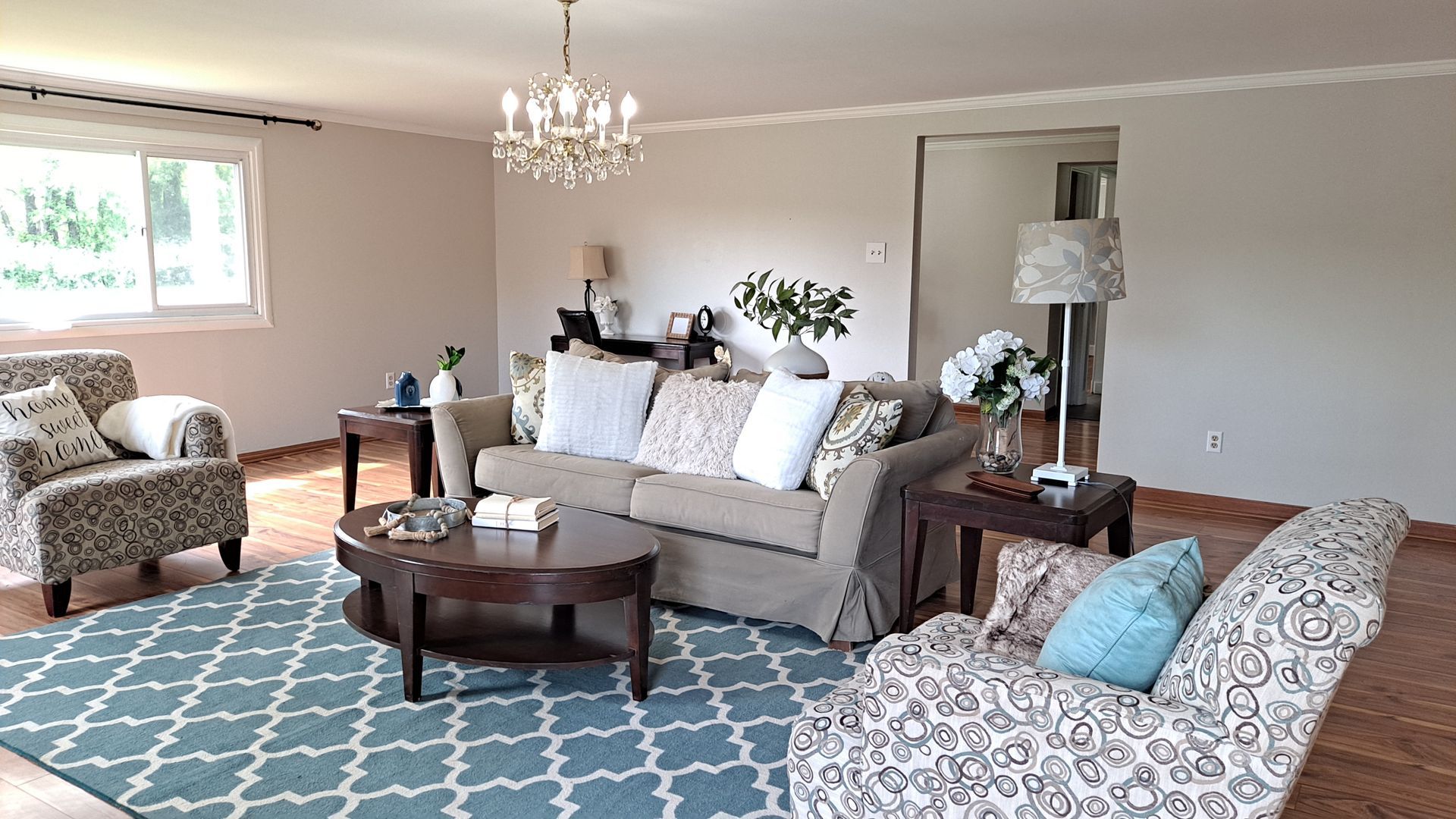 Living room with a sofa, two patterned chairs, a blue rug, and a chandelier.