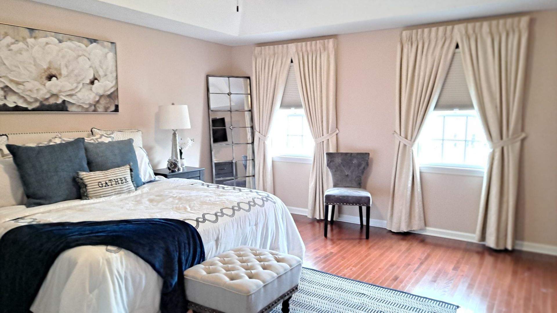 Bedroom with bed, tall mirror, two windows with curtains, and a chair.