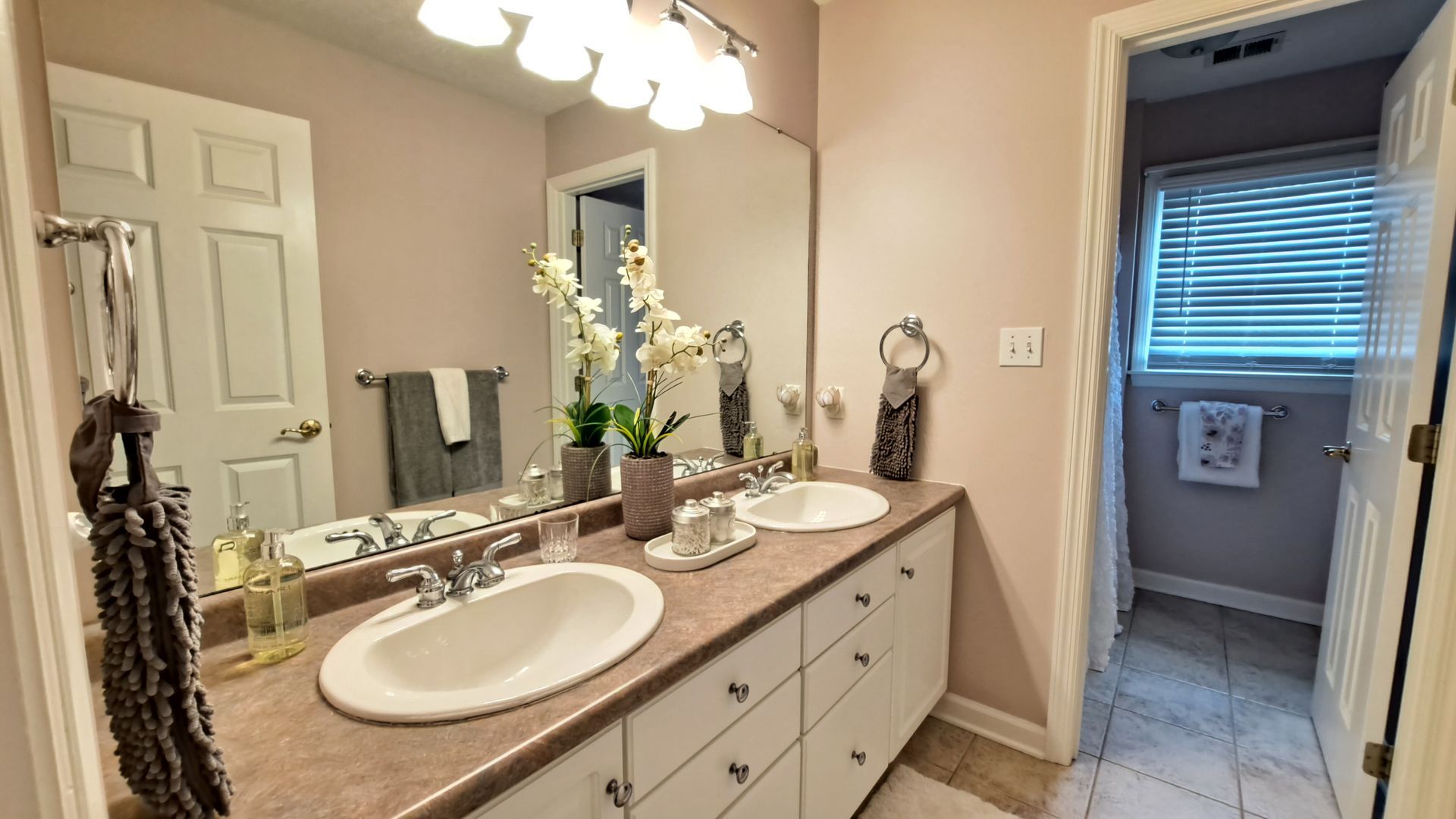 Bathroom with double sinks, mirror, and a view into a separate toilet area.