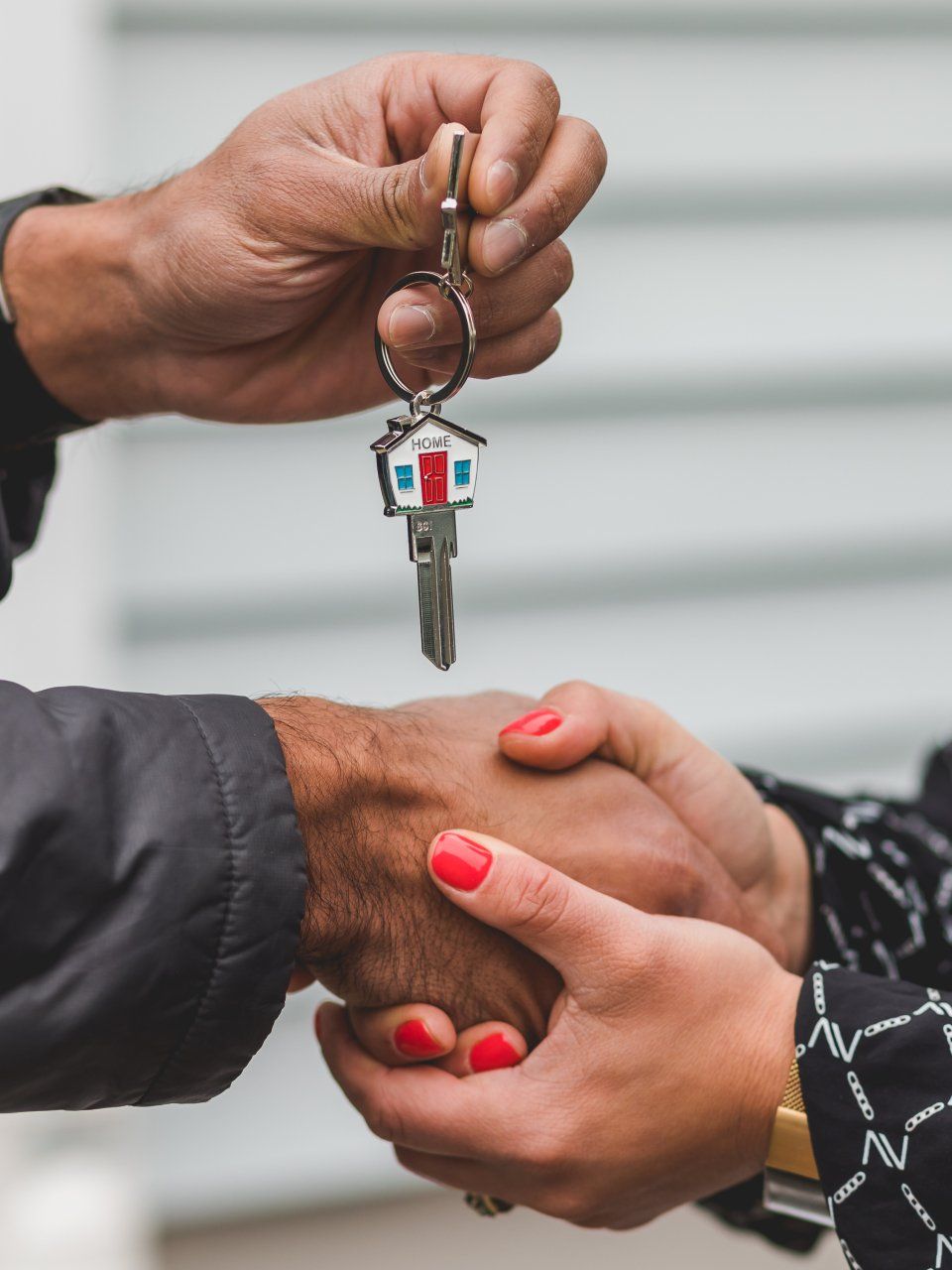 Person handing house key to another person, shaking hands.
