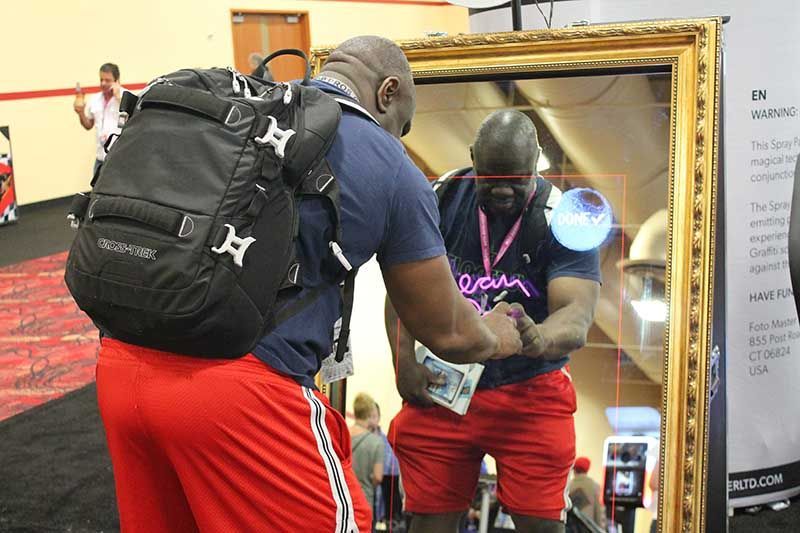 Man in red shorts and blue shirt looking in a mirror, wearing a backpack.