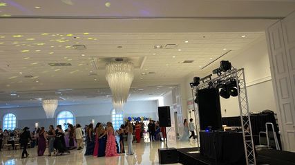 Large ballroom with people dancing. DJ setup in front; chandeliers and up-lighting visible.