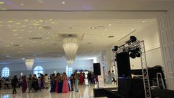Large ballroom with people dancing. DJ setup in front; chandeliers and up-lighting visible.
