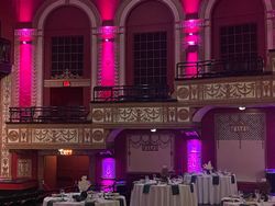 Pink-lit theater interior with balconies, tables, and ornate decorations.
