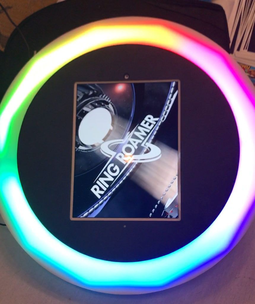 Ring Roamer photo booth with a glowing rainbow light ring. The booth has a screen displaying its logo.