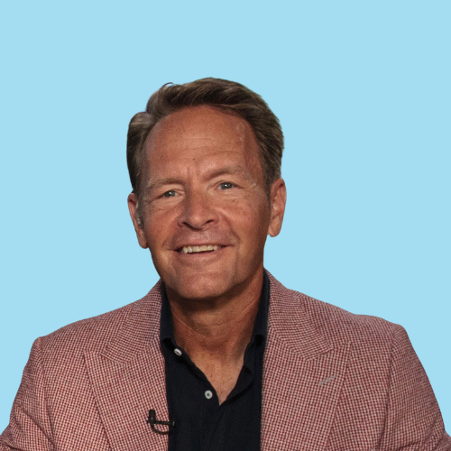 Man in a pink blazer smiles at the camera against a light blue backdrop.