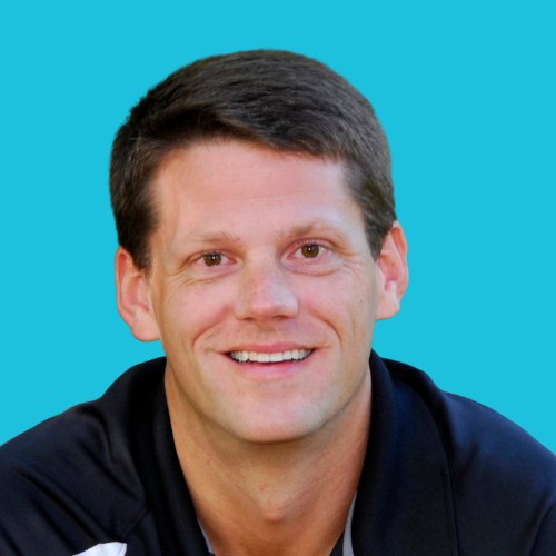 Man with short brown hair smiles, wearing a dark blue shirt against a turquoise background.