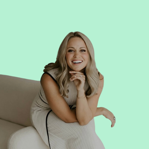 Woman with blonde hair smiling and leaning on a white couch. Light green background.