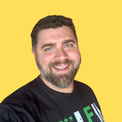 Smiling man with a beard in a black t-shirt against a yellow background.