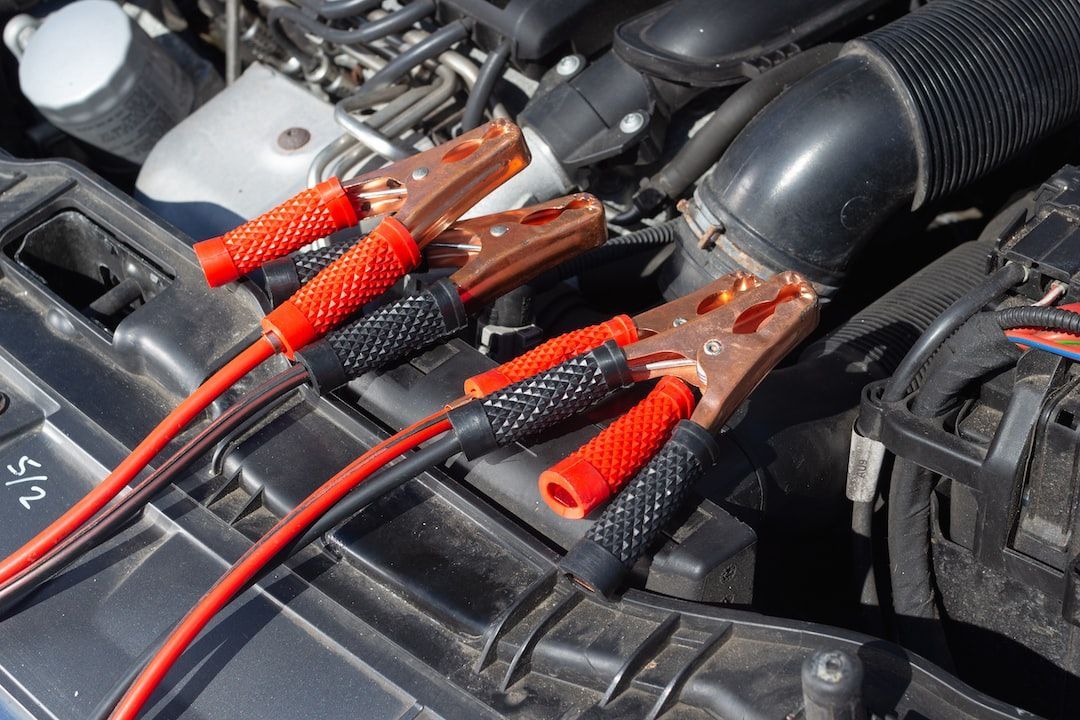 Red and black jumper cables connected to a car battery in an engine bay.