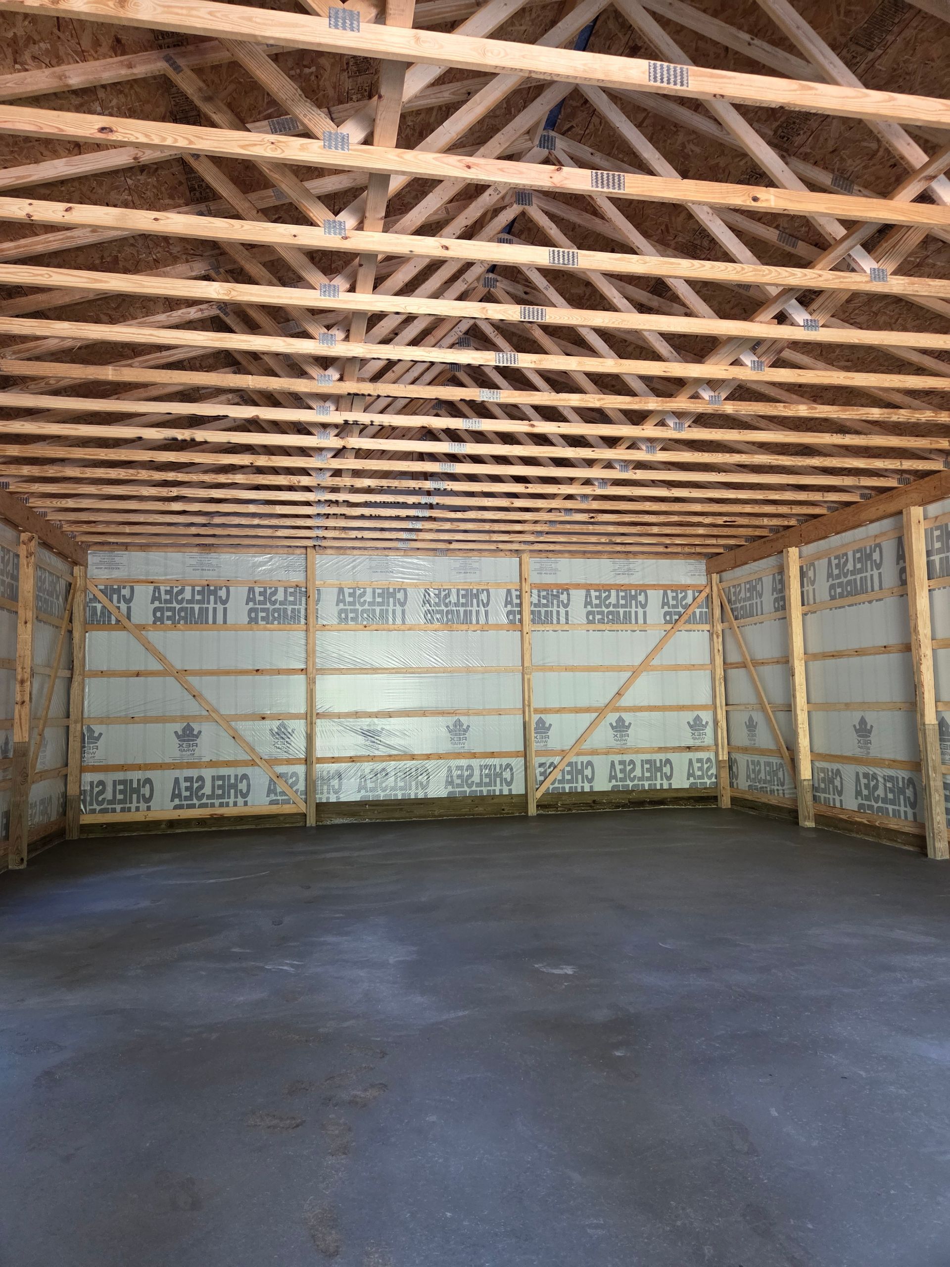 Interior of a partially constructed building. Wooden beams frame the walls and ceiling. Dark gray concrete floor. Insulation visible on the walls.