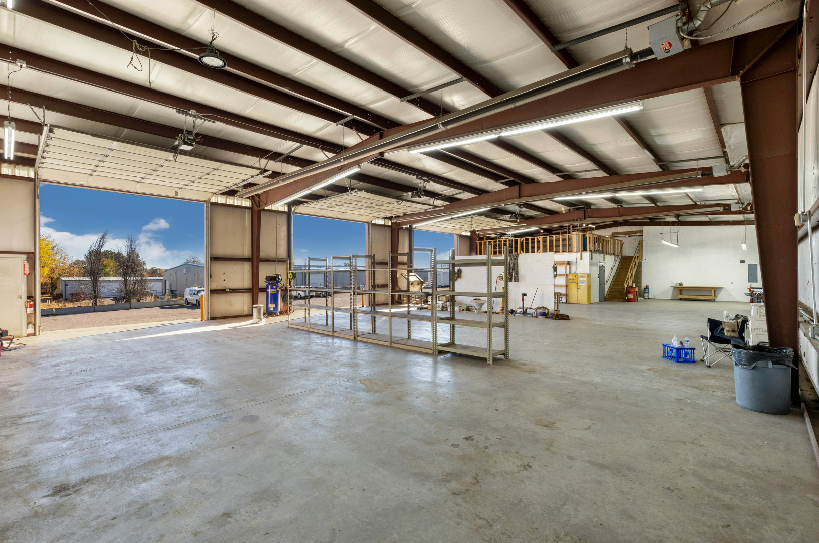 Empty industrial warehouse with open bay doors. Concrete floor, metal beams, and bright overhead lighting.