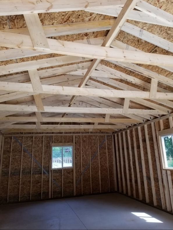 Interior view of a new building under construction: wooden roof trusses and walls with two windows, floor is concrete.