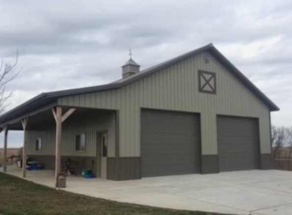 Tan and brown barn with two garage doors, a carport, and a cupola, set against a cloudy sky.