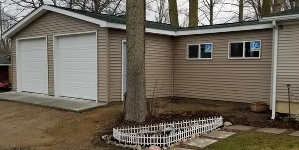 Tan house with two garage doors and two windows, a tree in front of the building.