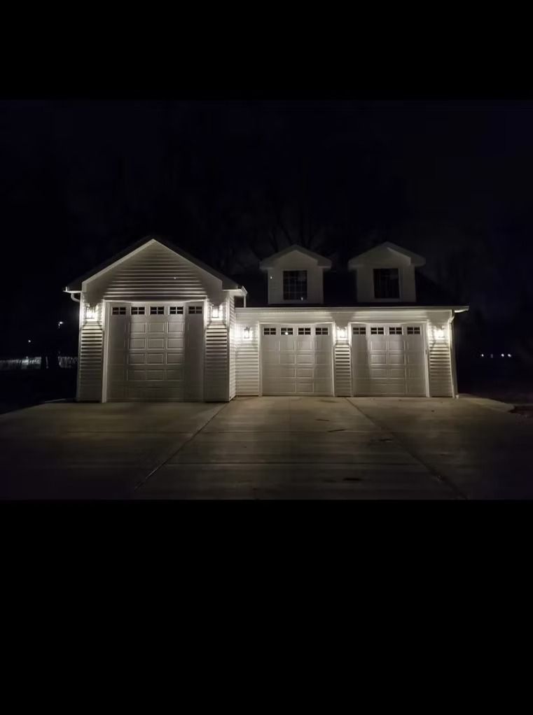 Nighttime view of a white garage with three doors, lit by outdoor lighting.