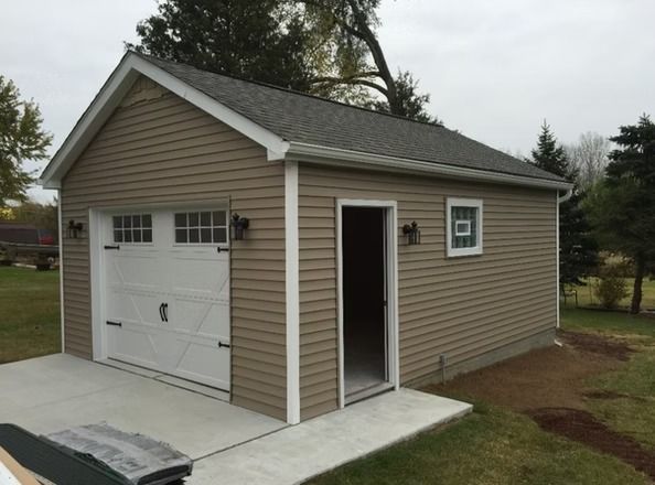 Tan garage with a white garage door and open door, set on a concrete pad, with landscaping in the background.