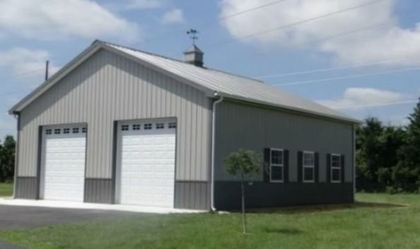 Two-bay gray metal garage with white doors, dark gray bottom, and black shutters against a blue sky.